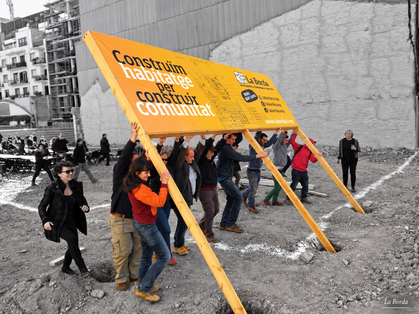Abitanti di La Borda sollevano uno striscione con la scritta «Construïm habitatge per construir comunitat» nel cantiere della cooperativa